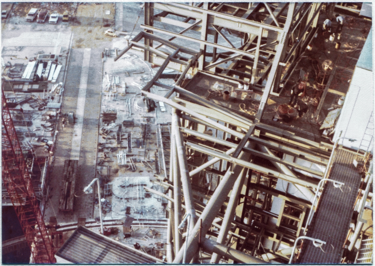 Image 008. Viewed from above on the Fixed Service Structure, the steel framework of the Rotating Service Structure at Space Shuttle Launch Complex 39-B, Kennedy Space Center, Florida, grows and takes shape as Union Ironworkers from Local 808, working for Wilhoit Steel Erectors, continue to work on it. In the distance, down on the ground, Wilhoit’s “shake-out yard” can be seen, straddling the western pair of tracks which are used by the Crawler, to transport the Mobile Launch Platform with the Shuttle on top of it to its launch position on the pad. Photo by James MacLaren. Image 008. Viewed from above on the Fixed Service Structure, the steel framework of the Rotating Service Structure at Space Shuttle Launch Complex 39-B, Kennedy Space Center, Florida, grows and takes shape as Union Ironworkers from Local 808, working for Wilhoit Steel Erectors, continue to work on it. In the distance, down on the ground, Wilhoit’s “shake-out yard” can be seen, straddling the western pair of tracks which are used by the Crawler, to transport the Mobile Launch Platform with the Shuttle on top of it to its launch position on the pad. Photo by James MacLaren.